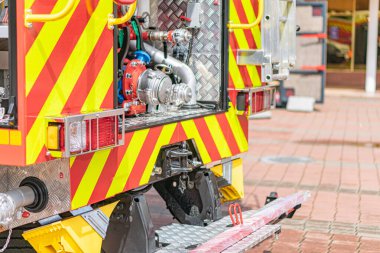 Sarı ve kırmızı bir itfaiye aracının görüntüsü. Tuğla bir yolda, yansıtıcı işaretler ve büyük bir pompayla donatılmış..