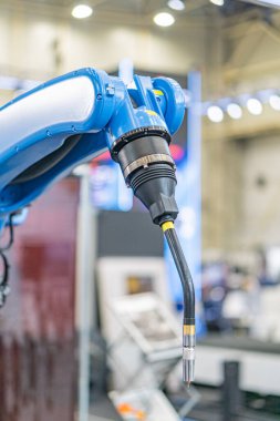 Hareket halindeki endüstriyel robot, birden fazla eklemli metalik kol ve matkap ucu montajı, yanan alanları ve gölgeleri zıtlaştıran yapay ışıklandırma, endüstriyel makineleri gösteren arka plan,