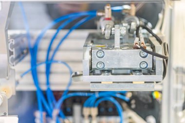 Endüstriyel makine, metalik çerçeve, cıvatalar, kablolama, insan eli, hassas mekanizma, elektrik bağlantıları, gölgeli parçalar, gri-mavi renk paleti