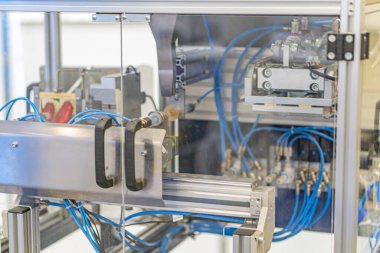 Çoklu bileşenli büyük metal makine, büyük ihtimalle hassas üretim ekipmanları, endüstriyel bir sahnede mavi hortumlar, kablolar, kablolar, beyaz konnektörler, anahtarlı panel, zma