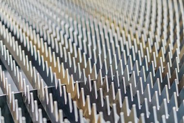 Düz bir yüzey üzerindeki küçük metal iğnelerden oluşan bir ızgaranın yakın görüntüsü, düzenli sıra ve sütunlar halinde dizilmiş, elektronik devre levhasını veya soğutma ısıtıcısını anımsatıyor.