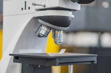 Endüstriyel arka planda aydınlatma yeteneğine sahip beyaz ve siyah bir mikroskobun yakın görüntüsü.