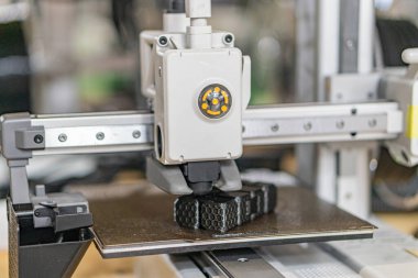 Sanayi ortamında bir 3D yazıcının yakın görüntüsü, hareket halindeki bir robotik kolu ile Sarımsı tutucu öne çıkıyor Beton zemin, metal çalışma istasyonu, bastırılmış aydınlatma, metalik tonlar, gerçekçi stil