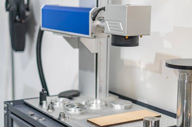Görüntü, yapay ışık altında mavi kapaklı büyük bir endüstriyel metal makineyi gösteriyor. Makine ayarlanabilir kollara ve saplara sahip, hassasiyet kontrolü öneriyor.