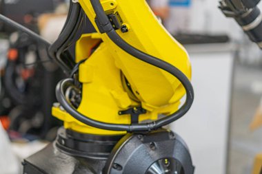 Metalik bir ortamda, güç kutusuna bağlanan eklem ve kablolarla donatılmış sarı endüstriyel robot kolunun yakın çekimi..
