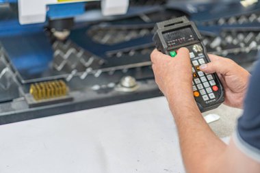 Ağır makineler ve yapay ışıklandırma ile kapalı bir çalışma alanında, makineler veya ekipmanlar için el bilgisayarı kullanan kişi