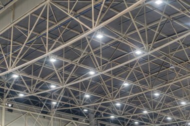 Geniş bir endüstriyel alan, yüksek tavanı, metal kirişleri, floresan ışıkları, yumuşak gölgeleri, beton yüzeyi ve görülebilir bir bağlam yok.