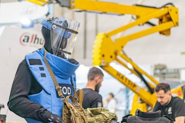 Koruyucu giysili portakallı kask, mavi çizgili ve renkli vizörlü kask, beyaz solunum maskesi, sanayi ortamında göğüste büyük makineli ikinci şahıs...