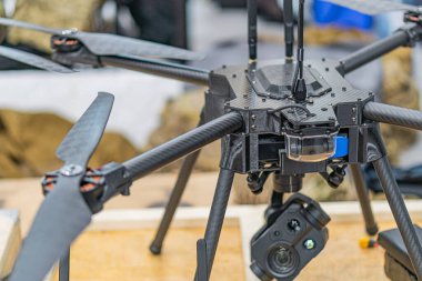 Siyah beyaz Ukrayna FPV insansız hava aracının yakın plan görüntüsü, pervaneleri genişletilmiş ve kamera pervanesi eklenmiş, arka planda bitki örtüsü olan açık hava kayalık ayarı eklenmiş.