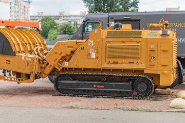 Asfaltlı alanda büyük sarı buldozer, kırmızı ve gri tuğlalar, raylar, kontroller, paneller, ağır iş makinesi, bulutlu gün, yumuşak gölgeler, bina arka planı, ağaçlar, elektrik hatları