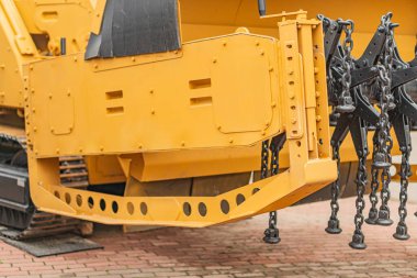 Turuncu ışık ve vinç eklentisi olan sarı bir inşaat aracının yan açısı doğal gün ışığı altında yeşilliğin yakınında yer almaktadır.