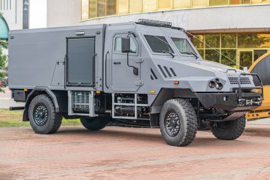 Modern zırhlı araç şehir merkezinde park halinde. Gri, havalandırma ve eklenti noktaları olan sağlam bir tasarım. Ağır lastikler, off-road yetenekleri.,