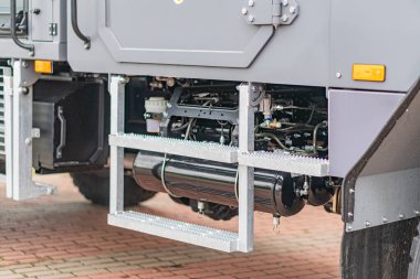 Gri zırhlı mayın temizleme aracı, modifiye edilmiş yatak ve ilave ekipmanlarla, kırmızı tuğla zeminde, bulutlu bir günde.