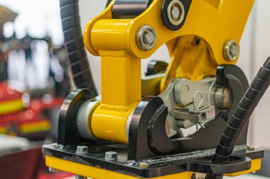 Bir montaj ortamında sarı ve siyah endüstriyel robot kolu, eklemli eklemleri, yapay ışıklandırması ve bulanık arka planı diğer makineleri işaret ediyor.