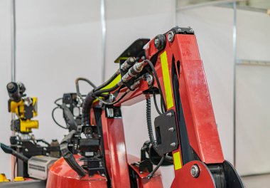 Büyük kırmızı bir robotik kol, çoklu eklentiler ve parlak ışıklandırılmış çalışma alanında gözlemcilerin yer aldığı endüstri sahnesi.
