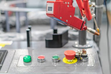 Kontrol panelinin üzerinde kırmızı robotik kolu olan sanayi ayarı, yapay ışıklandırma, metalik makine parçaları, fabrika veya atölye arka planı
