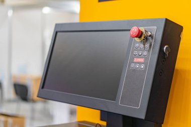 Endüstriyel ortamda büyük sarı metal bir makinenin yakın görüntüsü, bir kontrol paneli ve kısmen görünür mavi üniformalı bir işçi