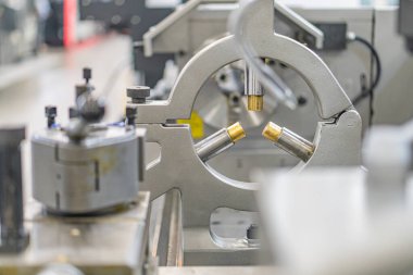 Büyük, gri metalik bir endüstriyel makine. Kolları, dişlileri ve mekanik parçaları var. Kapalı bir fabrika ortamında..