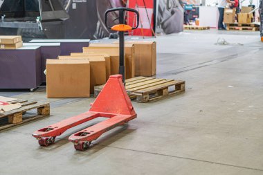 Kırmızı palet kamyonu, karton kutuları ve yapay aydınlatma altında beton döşemesi olan endüstriyel bir atölye veya fabrika.