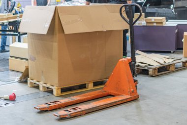 Depo sahnesi turuncu palet krikosu, ahşap paletler, karton kutular biri mühürlü, diğerleri boş, endüstriyel aydınlatma, sessiz toprak tonları