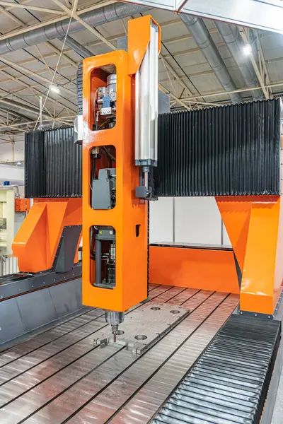 Fabrika zemininde turuncu ve siyah metal makine, silindir ve menteşeler, yüksek borular, cilalanmış beton, tepeden aydınlatma