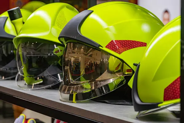 Parlak sarı itfaiyeci miğferleri bir mağaza duvarına karşı dizilmiş, soldan sağa sıralanmış çevreyi yansıtan vizörleri temizleyen açılı perspektif ipuçları bulanık p