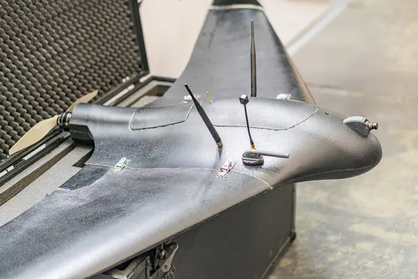 Sırtında desenli bir tabanı olan siyah bir dron. Görünür bileşenler arasında bir pil paketi, kontrol paneli ve eklentiler var. Yapay ışıklandırma bile güçlü gölgeler olmadan sahneyi aydınlatır.