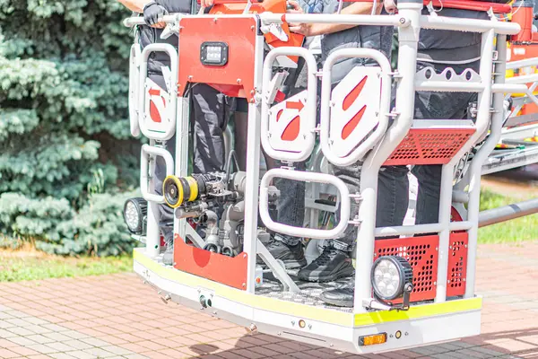 Gün ışığı sahnesi, itfaiye aracı asansörü, kırmızı ve beyaz makineler, vinç, koyu renk elbiseli iki operatör, görevlere odaklanmış, gerçekçi stil.