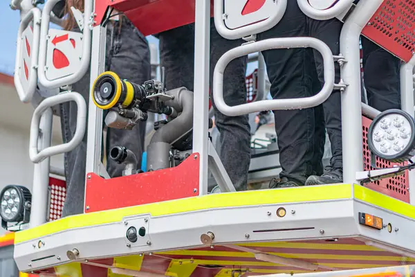 Kırmızı itfaiye aracı kaldırma sahnesi, acil müdahale, merdiven yukarı doğru uzanıyor, merdivende iki kişi, açık alan muhtemelen sokak, doğal ışıklandırma.