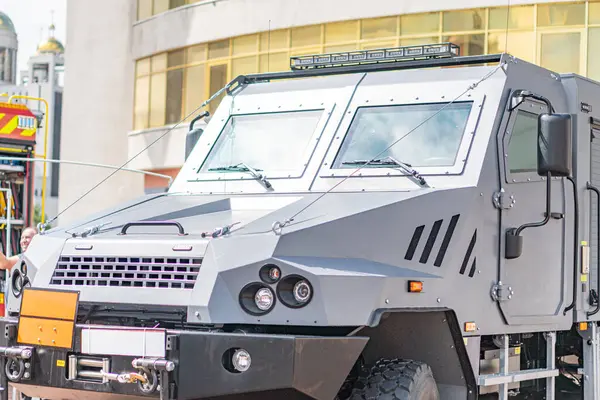 Şehir içi park edilmiş, kamuflajlı yeşil zırhlı personel taşıyıcı APC 'nin yan görüntüsü turuncu ön tamponu ve dört çekerli konfigürasyonu ile APC' nin görünür pencere veya kapısı yok Settin