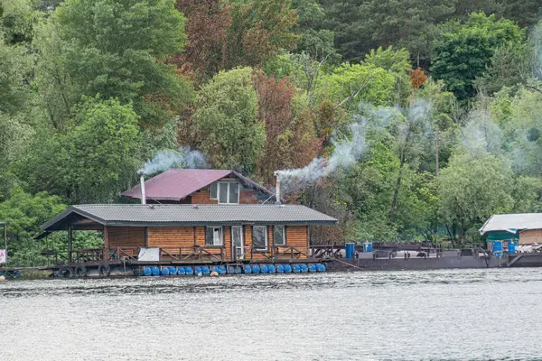 Rıhtımlı teknesi olan bir köy kulübesi bacadan görünür dumanlar ve yemyeşil doğa fotoğrafçılığı huzurlu şafak vakti sahnesini yakalıyor.