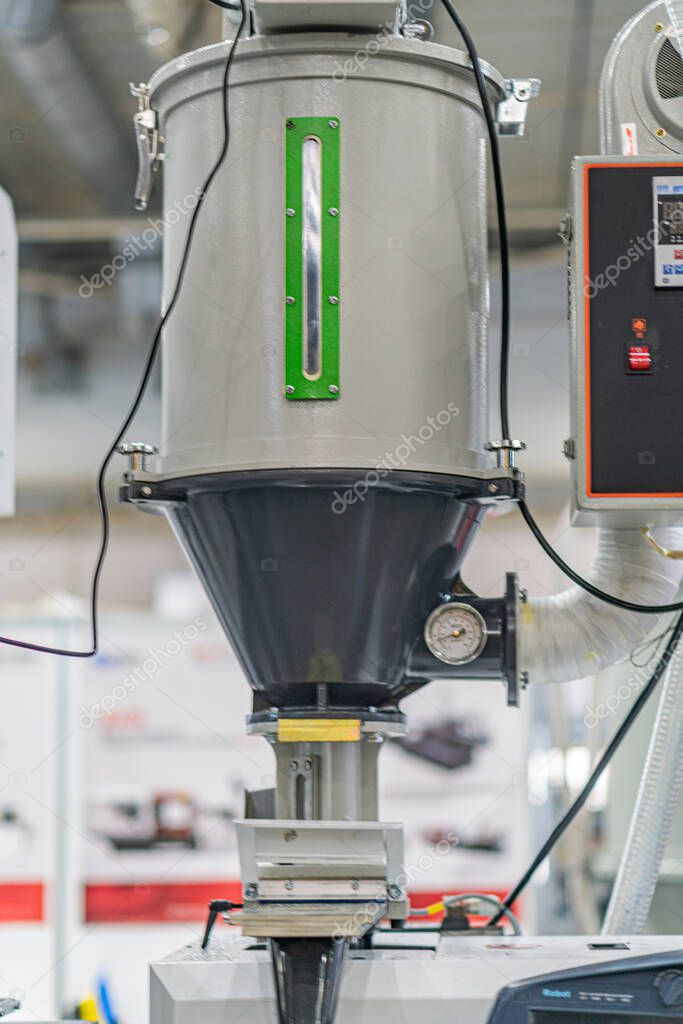 An industrial image features a large gray-green machinery dominating the foreground The complex setup includes cylindrical chambers, control panels, and mechanical components Background shows an in