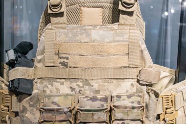 Koyu arkaplana karşı gösterimde zeytin yeşili savaş zırhı birden fazla ceple, fermuarla ve kamuflaj desenleriyle detaylandırılmış hiçbir metin veya insanlar nesneyi vurguluyor Sty