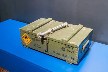 İçinde mühimmat bulunan yeşil metal bir askeri depo, mavi bir platforma yerleştirilmiş, hatta ışık altında, sarı tehlike etiketleri altında. a