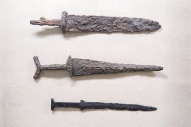 Üç antika kılıç, farklı boyutlarda, bej bir arka plana monte edilmiş süslemeli üst kılıç, basit orta kılıç, kullanışlı alt kılıç yaş ve işaretler kullanın paslı bıçaklar, renk değişimi yok yazı yok, kamış