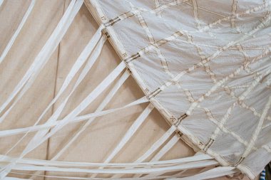Açık renkli bir ağ bölümünün yakın görüntüsü, muhtemelen ağlanmış paraşüt bileşeni, daha koyu dokulu yüzey. Kapalı ortamda ışık yayılıyor. İnsan veya metin yok.