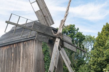 Kırsal, kırsal bir alanda eski ahşap yel değirmeni. Genişletilmiş bıçaklı, yemyeşil ağaçlarla çevrili ve açık mavi gökyüzü manzaralı doğal ışıklandırmalı.