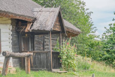 Yeşilliklerle çevrili, eski bir Orta Avrupa köyünde ahşap bir kulübe. Sazlı çatı yapısı kalasları, küçük bir penceresi ve kapının yanında bir bank var. Doğal, yayılmış ışık.