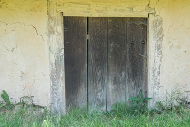 Eski bir Orta Avrupa köyünde harap olmuş ahşap bir ev. Kapalı bir kapı ve gözle görülür çürüme belirtileri var. Üs çevresindeki zemin düzensiz ve otlarla kaplı.