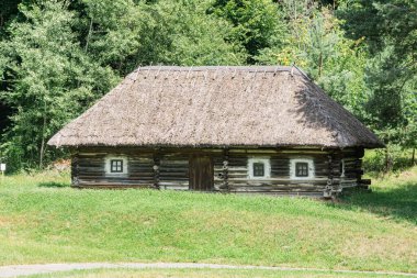 Doğal, kırsal ya da vahşi bir yerde eski bir kütük kulübe sazdan çatısı ve iki penceresi olan kırsal bir yapı kuruyor. Yeşillik, kahverengilik ve mavilerden oluşan doğal renk paletiyle gündüz vakti aydınlatılıyor. İnsan eylemi yok.
