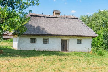 Eski Orta Avrupa sazdan çatılı bir ev, beyaz ve bej renkli, birden fazla penceresi ve kısmen açık ahşap kepenk parçalı bulutlu gökyüzü arkaplanı