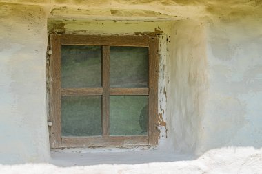 Soluk sarı bir Orta Avrupa binasının eski, yıpranmış penceresine yakın çekim, sessiz tonlu ahşap çerçeve, hafif dağınık ışık, yaşlanmış görünüm