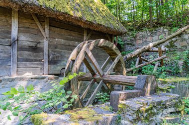 Antik Orta Avrupa köyü sahnesi, su çarklı ahşap yapı, yeşil yeşillik, gündüz aydınlığı, toprak tonları, hiç insan yok.