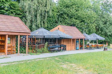 Orta Avrupa 'nın eski bir köyünde, samanlı çatıları ve küçük tenteleri olan iki ahşap kulübenin yer aldığı sakin bir açık alan yakınlarda dört siyah şemsiye gruplandırılmış, zıt tarımsal