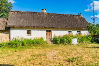 Tuhaf beyaz kulübe, yemyeşil, koyu kahverengi kiremitli çatı, birden fazla baca, gri ahşap kapı, iki pencere, canlı çiçekler, taş duvar, berrak mavi gökyüzü, parlak mavi bulutlar, huzurlu merkez