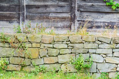 Orta Avrupa 'da bir köyde eski bir taş duvar, kısmen ahşap çitle kaplanmış duvar yıpranmış ve bitkisel büyümeye sahip yumuşak ortam aydınlatması bulutlu ya da gölgeli bir atmosfer yaratır.