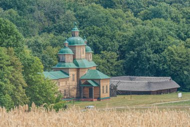 Eski Doğu Ortodoks Kilisesi, ilkbahar veya yaz aylarında Orta Avrupa 'nın kırsal bir köyünde yel değirmeni. Koyu çatı ve aydınlık duvarları olan geleneksel ahşap yapı, patika, mezar taşları, yemyeşil la