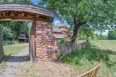 Antik Orta Avrupa köyü, kırsal cazibe, ahşap kemer yolu, taş bina, yeşil alan, uzun otlar, yumuşak doğal ışık, toprak renkler, sığ alan derinliği, bulutlu gökyüzü, gerçekçi stil.