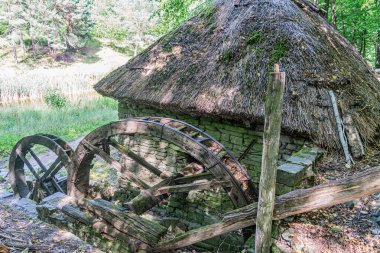 Orta Avrupa 'da sakin, eski bir su çarkı, kırsal ahşap yapı, yaş ve aşınma belirtileri, sazdan çatı, yosun bantları, yemyeşil, yumuşak ışıklandırma, yalnızlık, terk edilme, kişi başı yükseltilmiş.