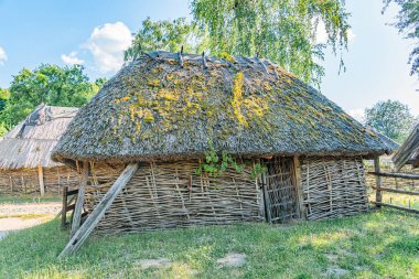 Konik sazdan çatı kulübesi, eski bir Orta Avrupa köyünde yer alan toprak bir ses tonunda. Yapı, ağaç ve bitki örtüsü de dahil olmak üzere doğal malzemelerden yapılmıştır.